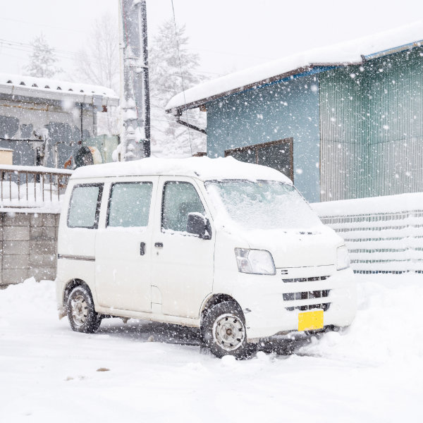 雪の降る街中を走行する配送車の冬期配達イメージ